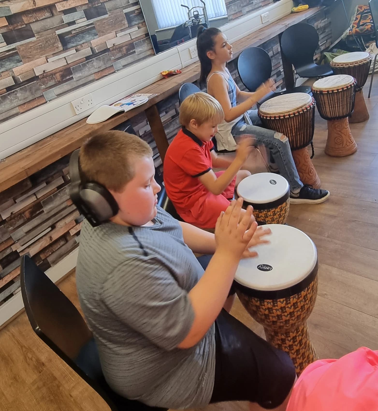 A picture of children practising on djembe drums during a session at the Community Centre during the school holidays.