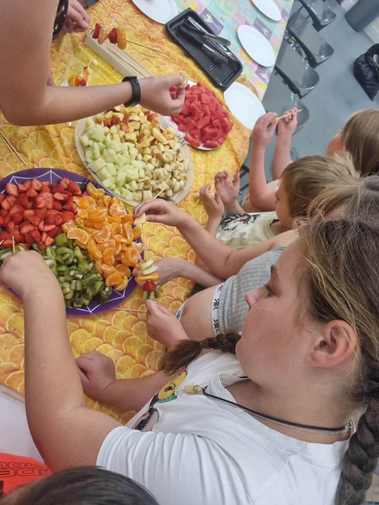 A picture of some young children making fruit kebabs at a community centre summer holiday session.